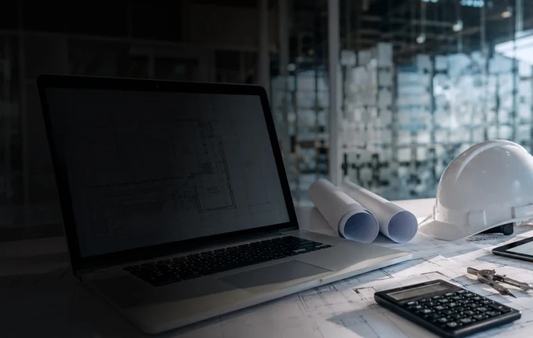 Planeación de proyectos con planos, casco de obra y laptop